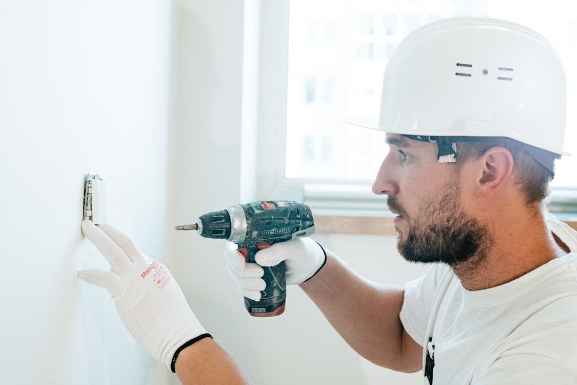 Professional handyman with hard hat using power drill on wall — same-day service from $129